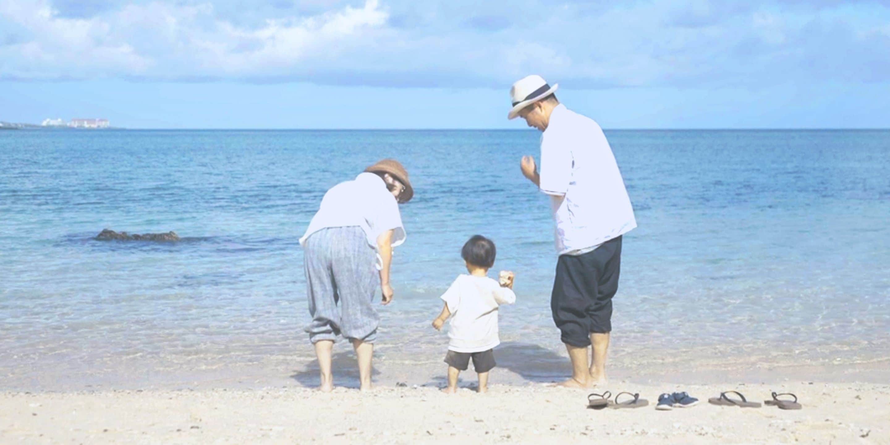 Escena de playa con tres personas, incluyendo un niño, cerca de la orilla.
