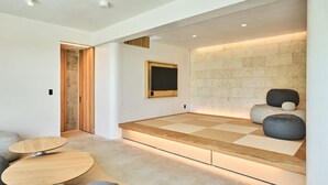 A modern room with a tatami mat seating area, a wooden table, and a stone wall. - ima villa (Onna)
