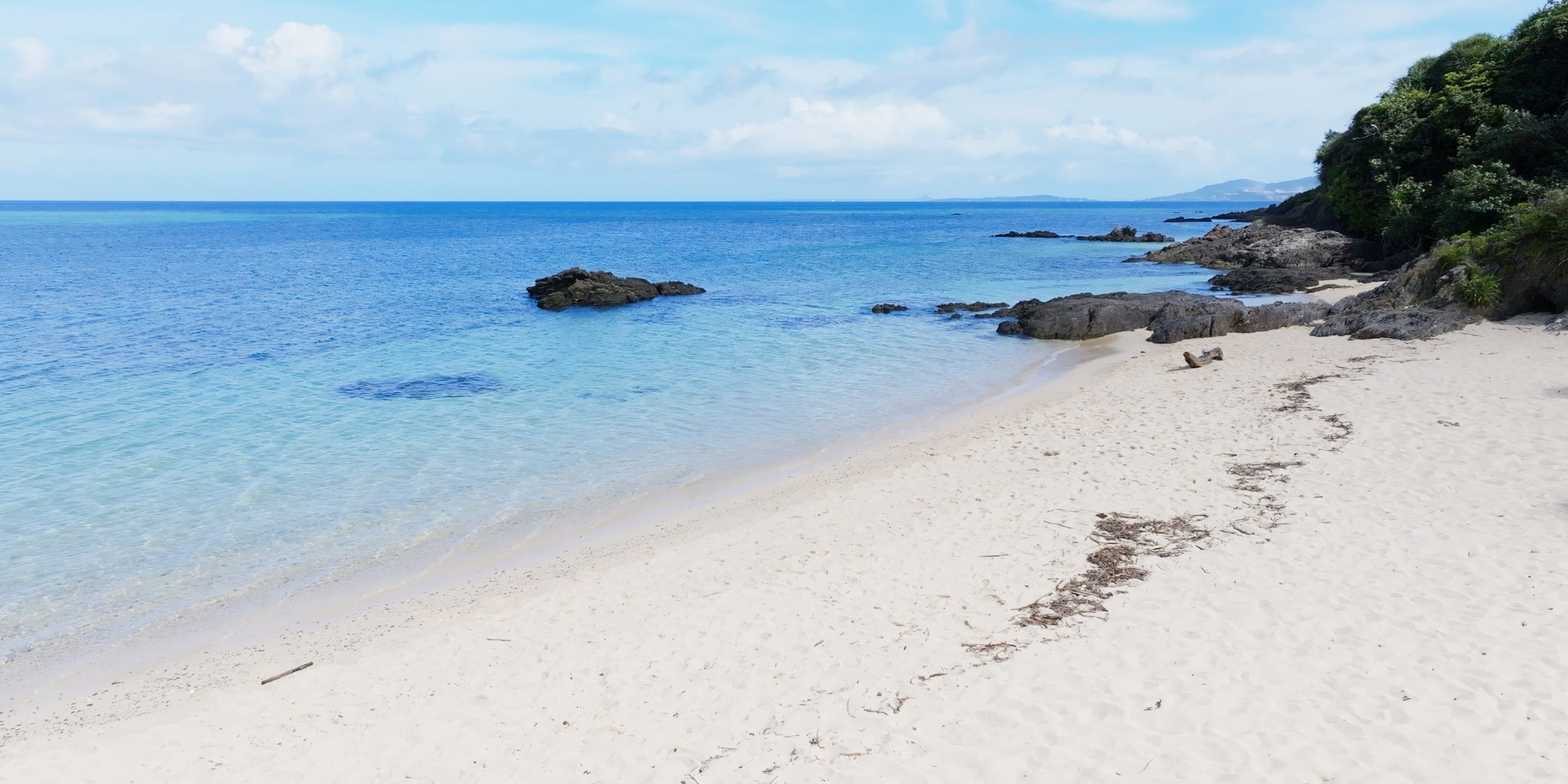 Una platja amb aigua clara i blava, sorra i roques.