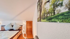 A bedroom with a bed, pillows, a headboard, a wall-mounted light, and a large landscape painting. - Apartment 'Fewo Zuckerfeld' with Shared Terrace and Wi-Fi (Gersfeld (Rhön))
