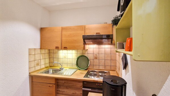 A compact kitchen with wooden cabinets, a sink, a stove, and a trash bin.