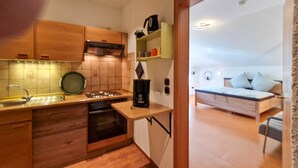 A compact kitchen with a stove, sink, and coffee maker, and a bedroom with a bed and bedside table. - Apartment 'Fewo Zuckerfeld' with Shared Terrace and Wi-Fi (Gersfeld (Rhön))