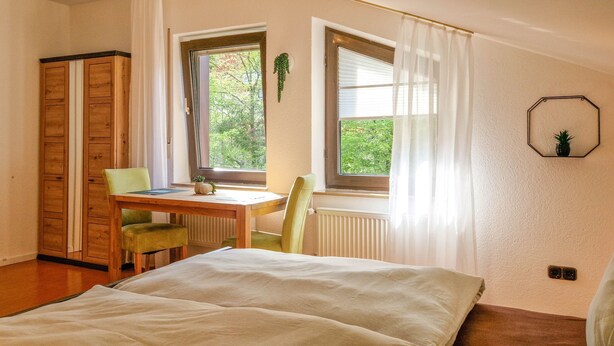 A bedroom with a bed, a desk, and a chair. There is a window with curtains, a radiator, and a door. - Apartment 'Fewo Zuckerfeld' with Shared Terrace and Wi-Fi (Gersfeld (Rhön))