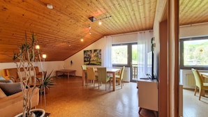 A spacious loft with a high ceiling, wooden beams, a dining area with chairs, a sofa, and a TV.
