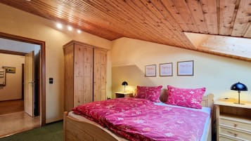 Ein Schlafzimmer mit Holzboden, einem Bett mit floralem Bettzeug, einem Nachttisch, einer Kommode und einer Tür zu einem anderen Raum.