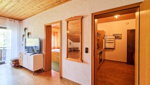 A room with a television, a desk, a bed, a mirror, and a kitchen area.