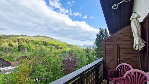 A balcony with a view of a green valley, wooden railing, and a white umbrella.