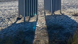 Two beach huts with striped awnings on a sandy beach with a clear sky and sun. - Apartment 'Meerzeit' with Sea View, Balcony and Wi-Fi (Eckernförde)