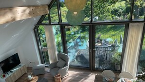 A modern living room with a large window, a TV, a sofa, a chair, a dining table set for two, and a small side table. - Apartment 'Meerzeit' with Sea View, Balcony and Wi-Fi (Eckernförde)
