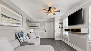 A living room with a gray sofa, a ceiling fan, a flat-screen TV, and artwork on the walls. - Fly-In Style: Charming Townhome 6 Mins from RIC! (Highland Springs)
