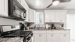 A modern kitchen with white cabinets, a stainless steel range hood, and a built-in oven. - Fly-In Style: Charming Townhome 6 Mins from RIC! (Highland Springs)