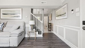 A living room with a grey sofa, a small table with a lamp, and a staircase leading to another room. - Fly-In Style: Charming Townhome 6 Mins from RIC! (Highland Springs)