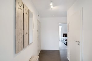 Un couloir avec un lambris en bois, une porte et un aperçu d’une chambre à coucher avec un lit et une fenêtre.