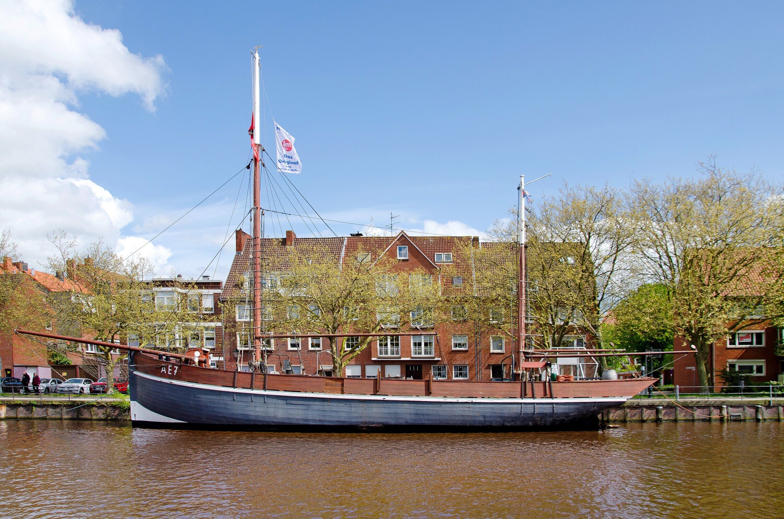 Un bateau en bois traditionnel est amarré à un canal, avec un bâtiment en briques rouges en arrière-plan.