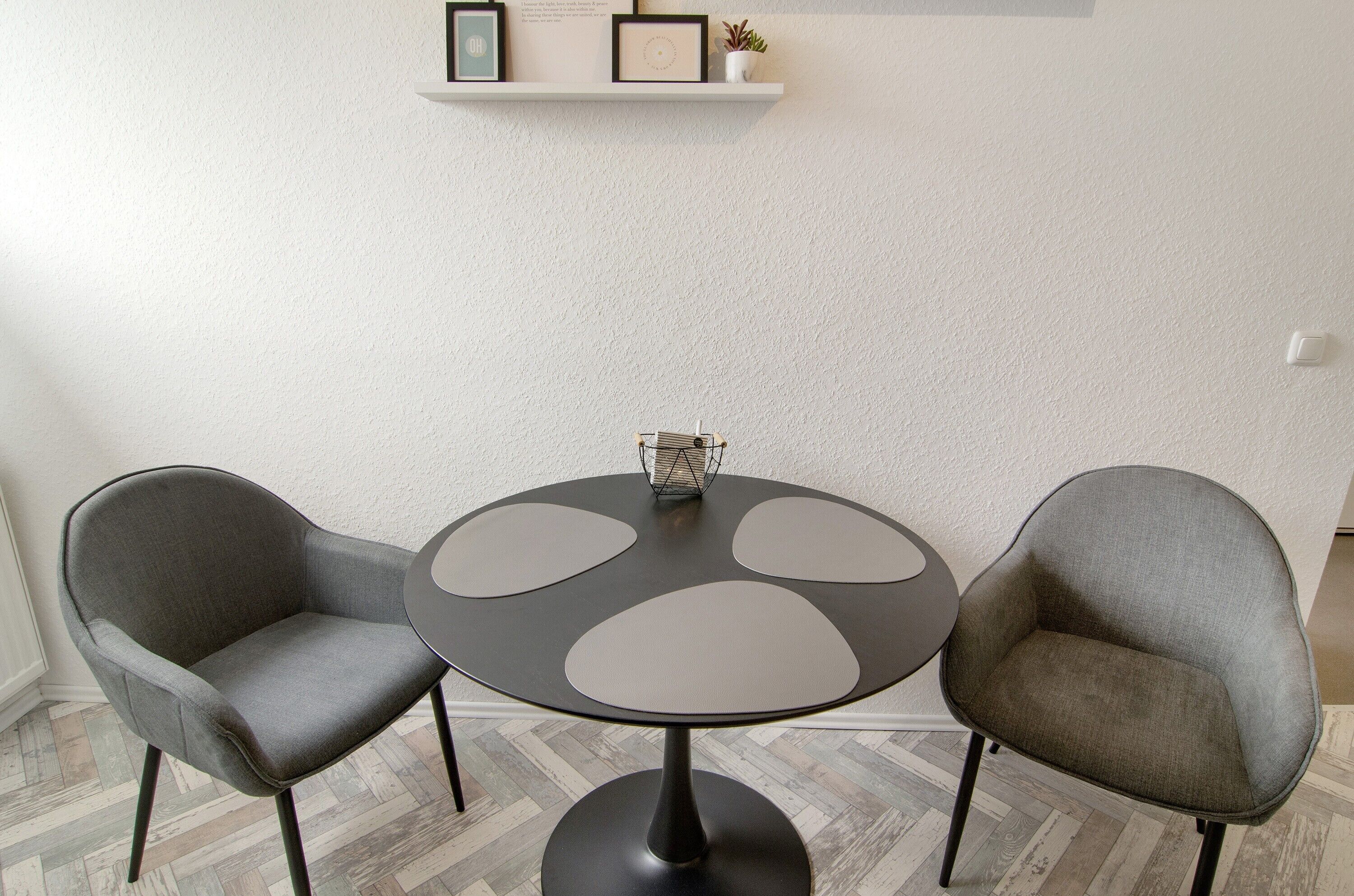 Een ronde tafel met een zwart onderstel en vier grijze, ronde uitsparingen, met aan weerszijden twee grijze fauteuils met zwarte poten.
