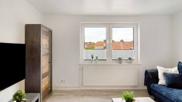A modern living room with a flat-screen TV, a dark blue sofa, a white radiator, and a window with blinds.