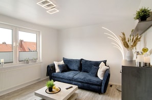 Un salon moderne avec un canapé bleu foncé, une table basse agrémentée d’une plante, une télécommande et un vase décoratif.