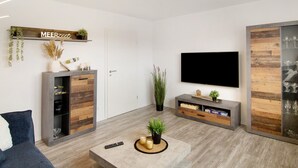 A modern living room with a TV, wooden shelving, and a minimalist design.