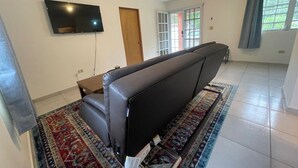 A living room with a sofa, a flat-screen TV, a door, and a window with curtains. - Where Bad Bunny is from - Cozy Mountain Valley Villa Vega Baja with AC, WiFi (Vega Baja)
