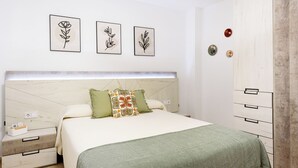 Ein Schlafzimmer mit einem Bett, Nachttischen, einem Kleiderschrank und drei gerahmten Pflanzenabbildungen an der Wand.