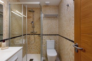 A bathroom with a glass shower enclosure, a white toilet, and a wooden door.