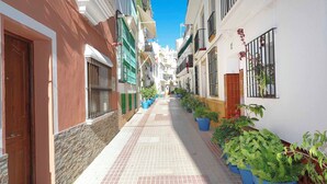 Eine schmale Straße mit Gebäuden an beiden Seiten, Blumentöpfen und blauem Himmel.