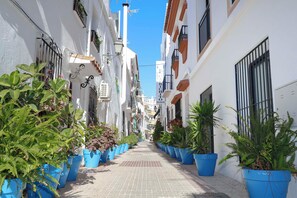 A narrow street lined with white buildings, blue planters, and a clear blue sky.