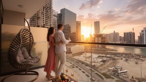 Una pareja parada en un balcón con vista a un paisaje urbano de edificios modernos y una vista al agua.