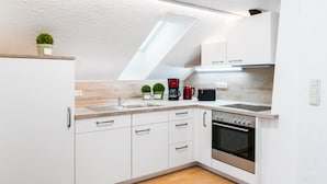 Una cocina moderna con armarios blancos, horno empotrado, cafetera y una pequeña planta en maceta.