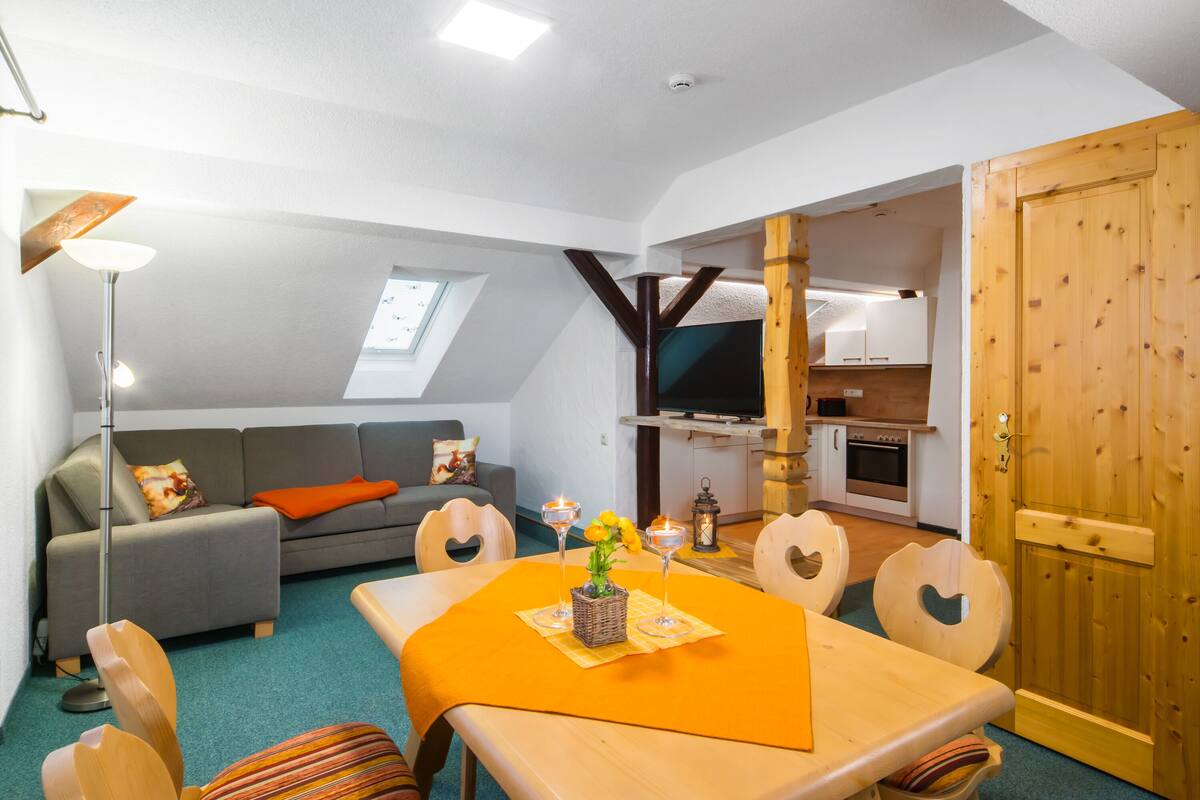 A cozy living room with a sofa, a dining table with chairs, a TV, and a kitchen area.