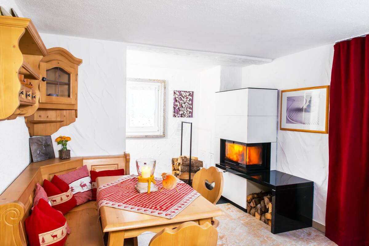 A cozy room with a wooden table, a sofa, a TV, a fireplace, and a red curtain.