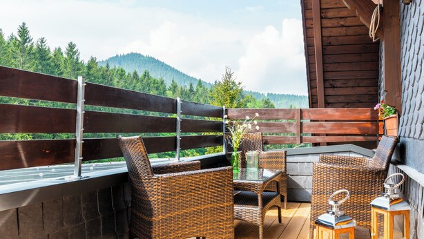 Una terraza de madera con mobiliario de mimbre, una mesa de vidrio y faroles.