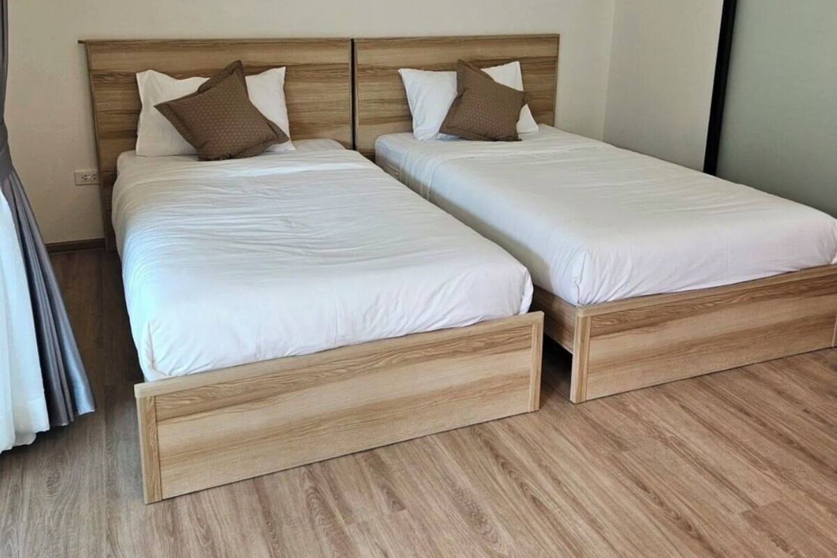 Un lit double avec une tête de lit en bois et deux oreillers, un plancher en bois et une fenêtre avec des rideaux.