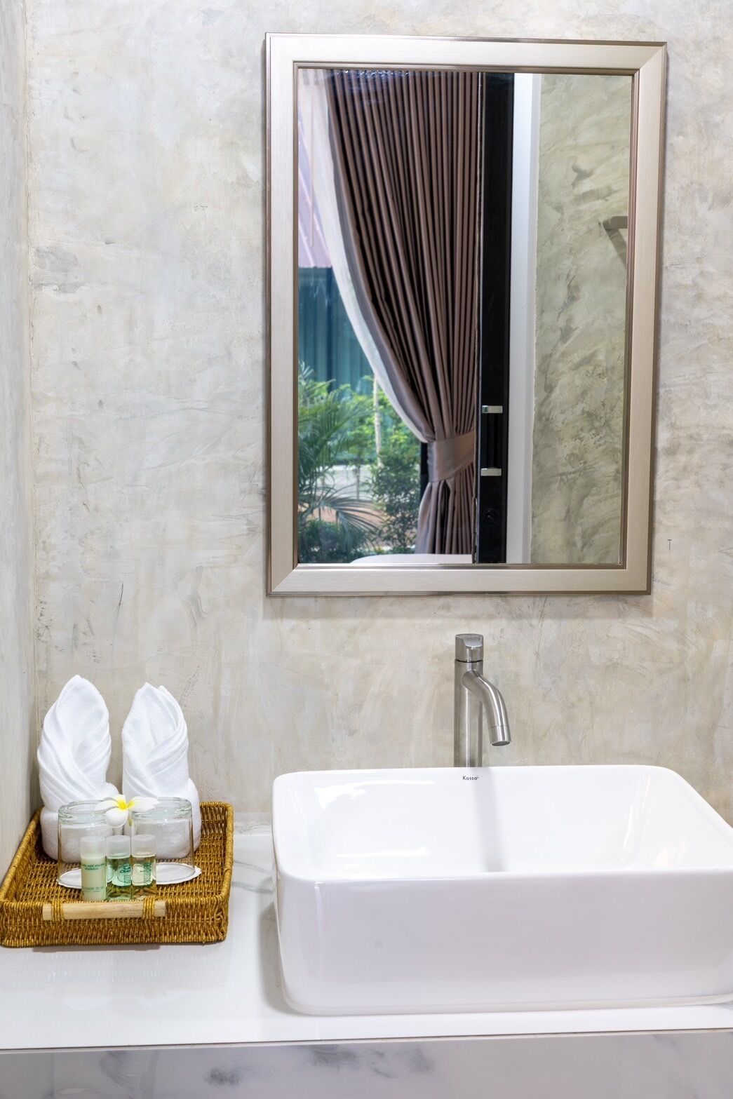 A bathroom with a white sink, a mirror, and a wicker tray with toiletries.
