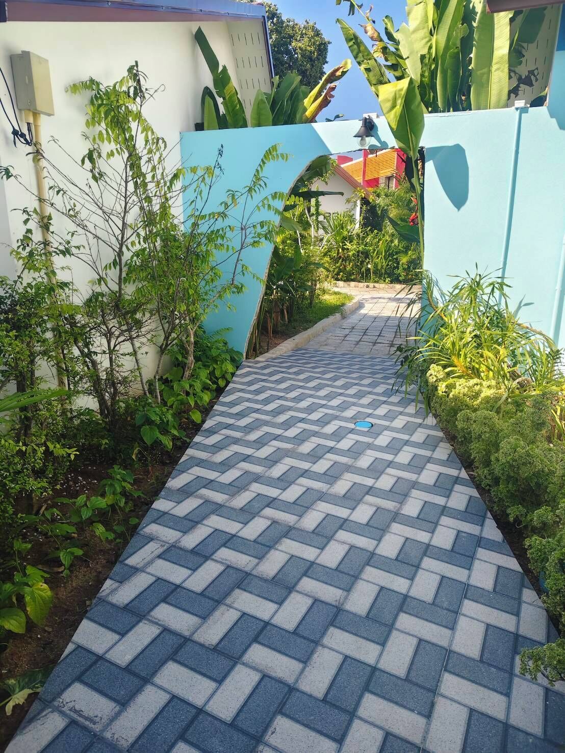 A paved pathway leading to a building with a blue wall and a white wall with a door.