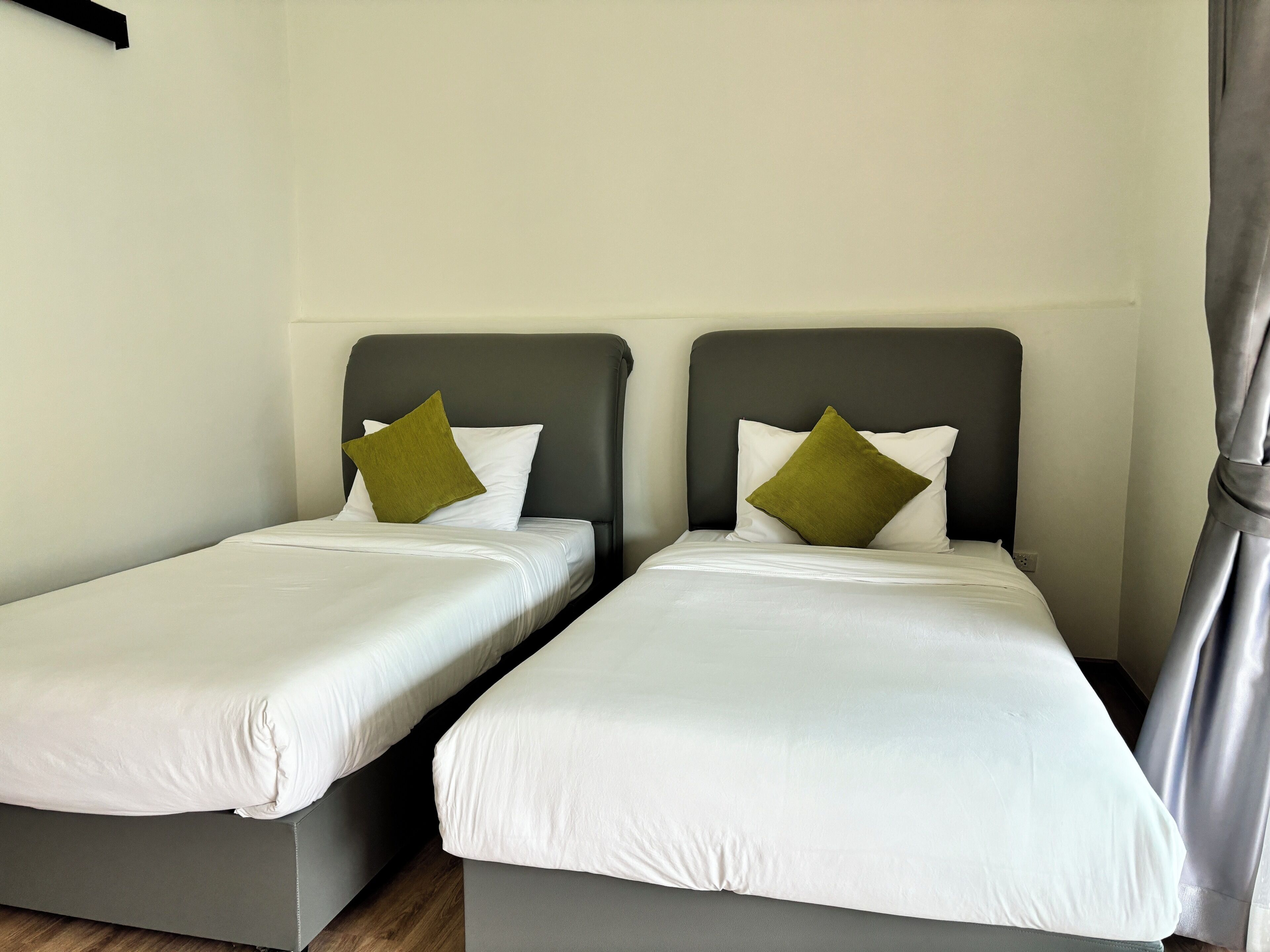 Two single beds with grey headboards and white bedding, a grey floor, and a plain white wall.