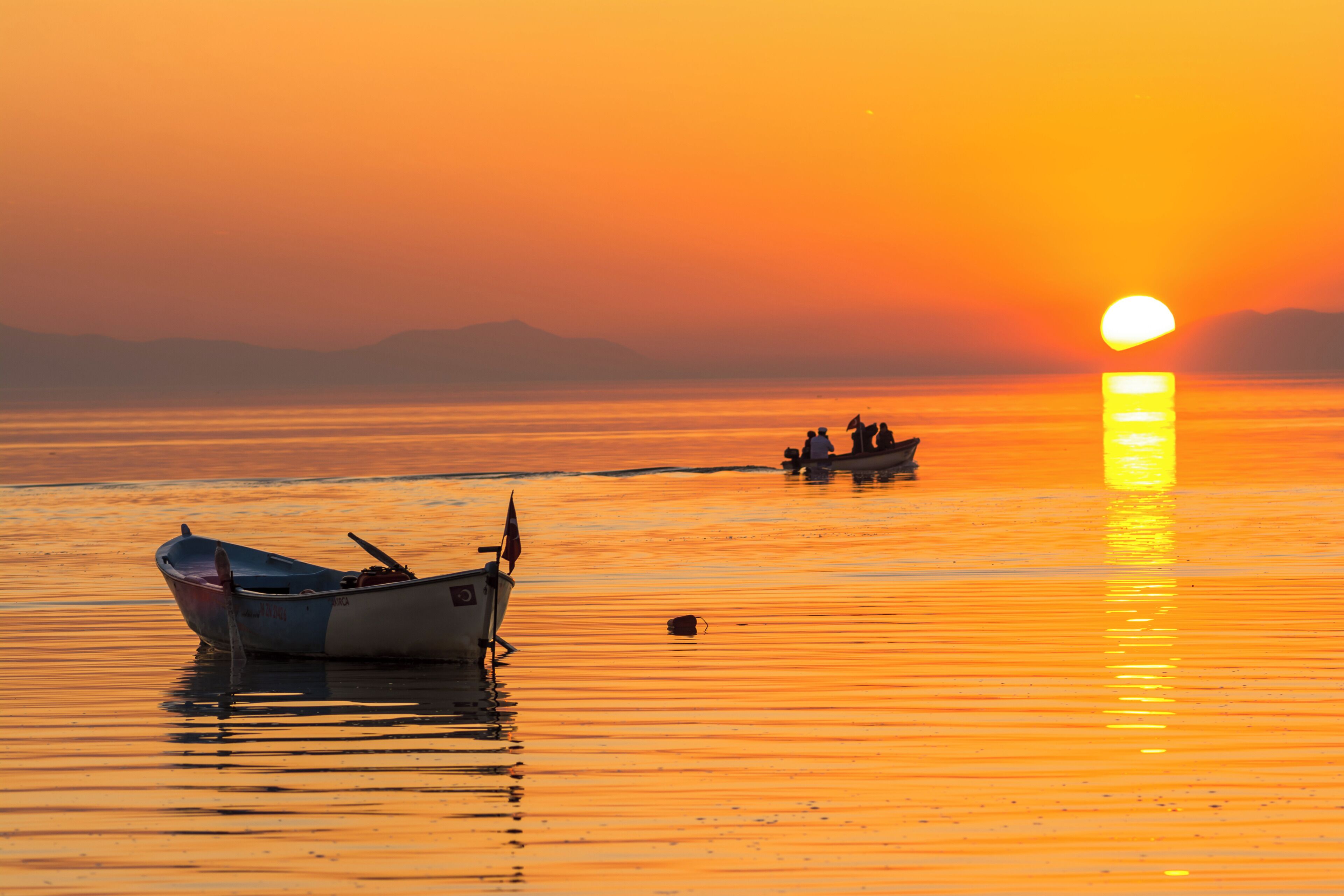 A calm body of water with boats and a sunset.