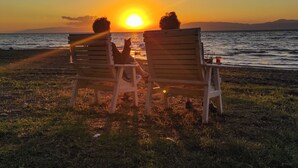 Dos sillas de madera mirando al atardecer sobre el agua, con montañas a lo lejos.