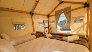 Una habitación tipo tienda de campaña con dos camas, una escalera y ventanas.