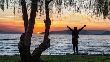A person standing by a lake at sunset with trees and mountains in the background.