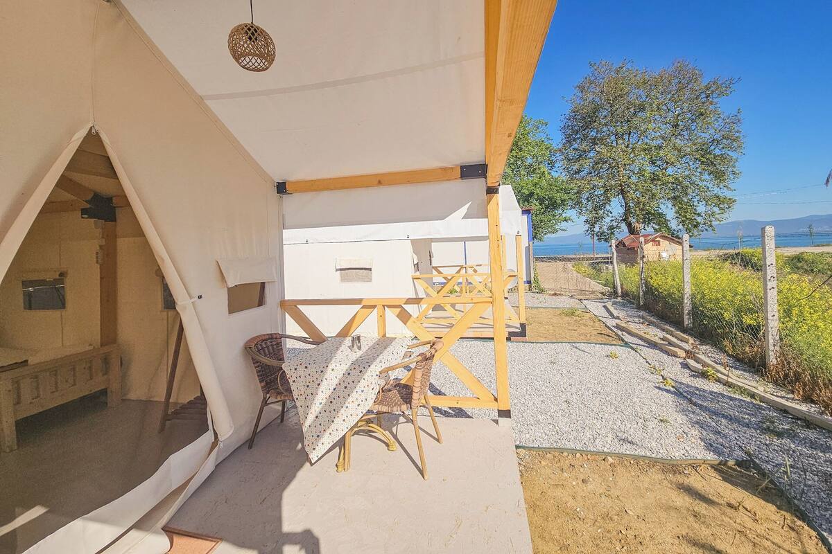 Alojamento em tenda com mesa e cadeiras, vista para o mar e estrutura de madeira.