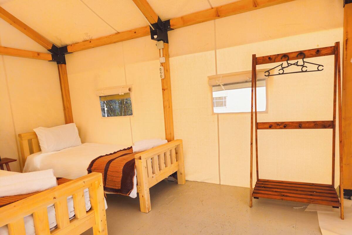 Quarto com duas camas de madeira, uma beliche e uma janela, além de estrutura de teto em madeira.