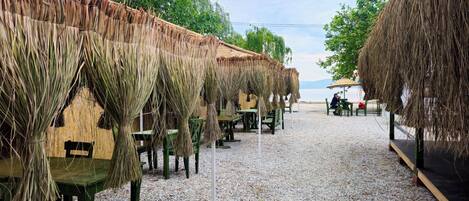 A beachside restaurant with thatched umbrellas and wooden tables.