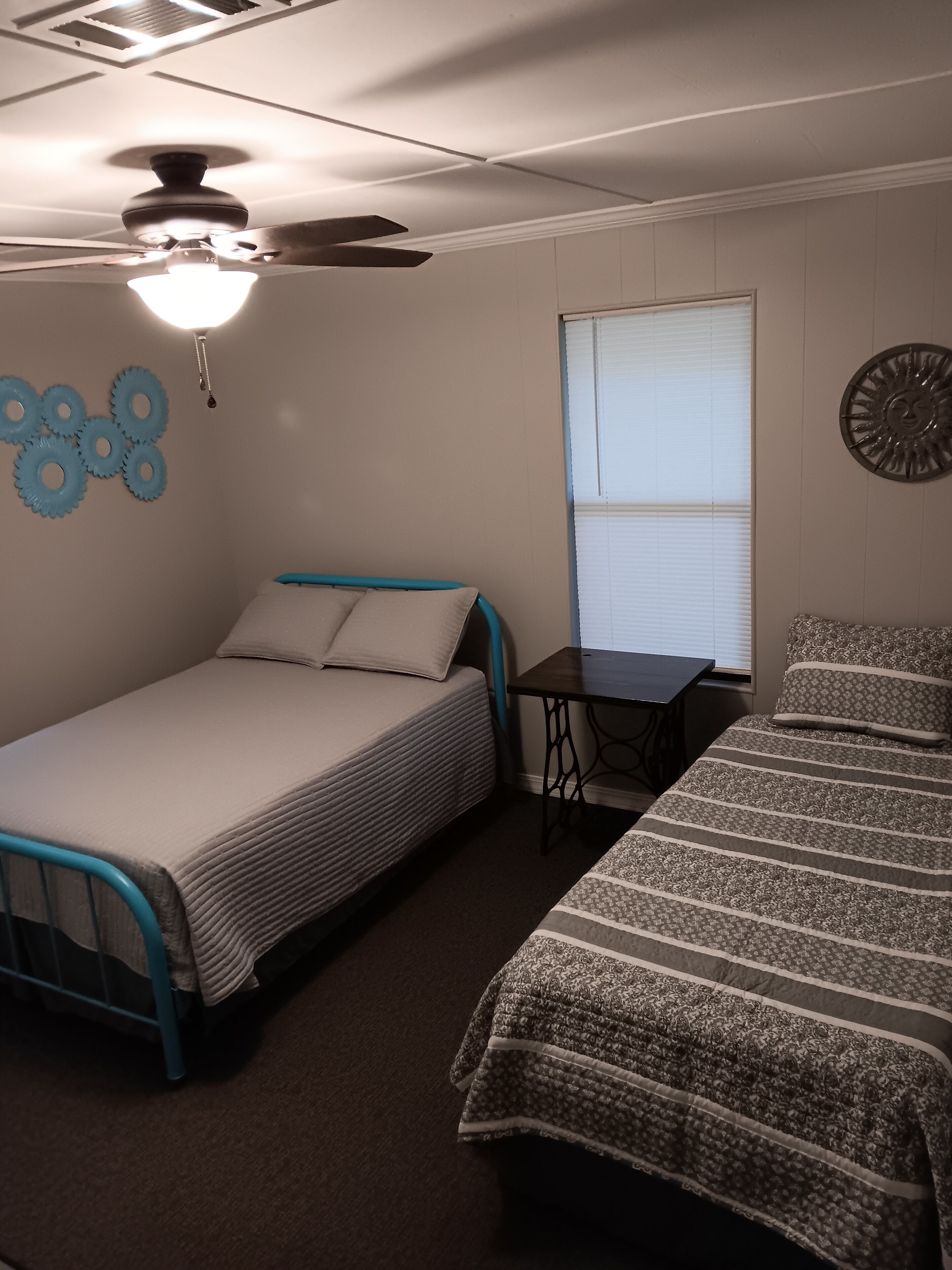 A bedroom with two beds, a ceiling fan, a window with blinds, and a wall clock.
