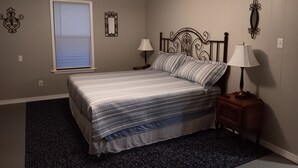Une chambre à coucher comprenant un lit, une table de chevet, une lampe, un ventilateur de plafond, une fenêtre avec des stores et des miroirs décoratifs sur les murs.