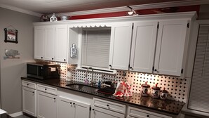 Une cuisine avec des meubles blancs, un plan de travail noir, un four à micro-ondes, un évier et des objets décoratifs.