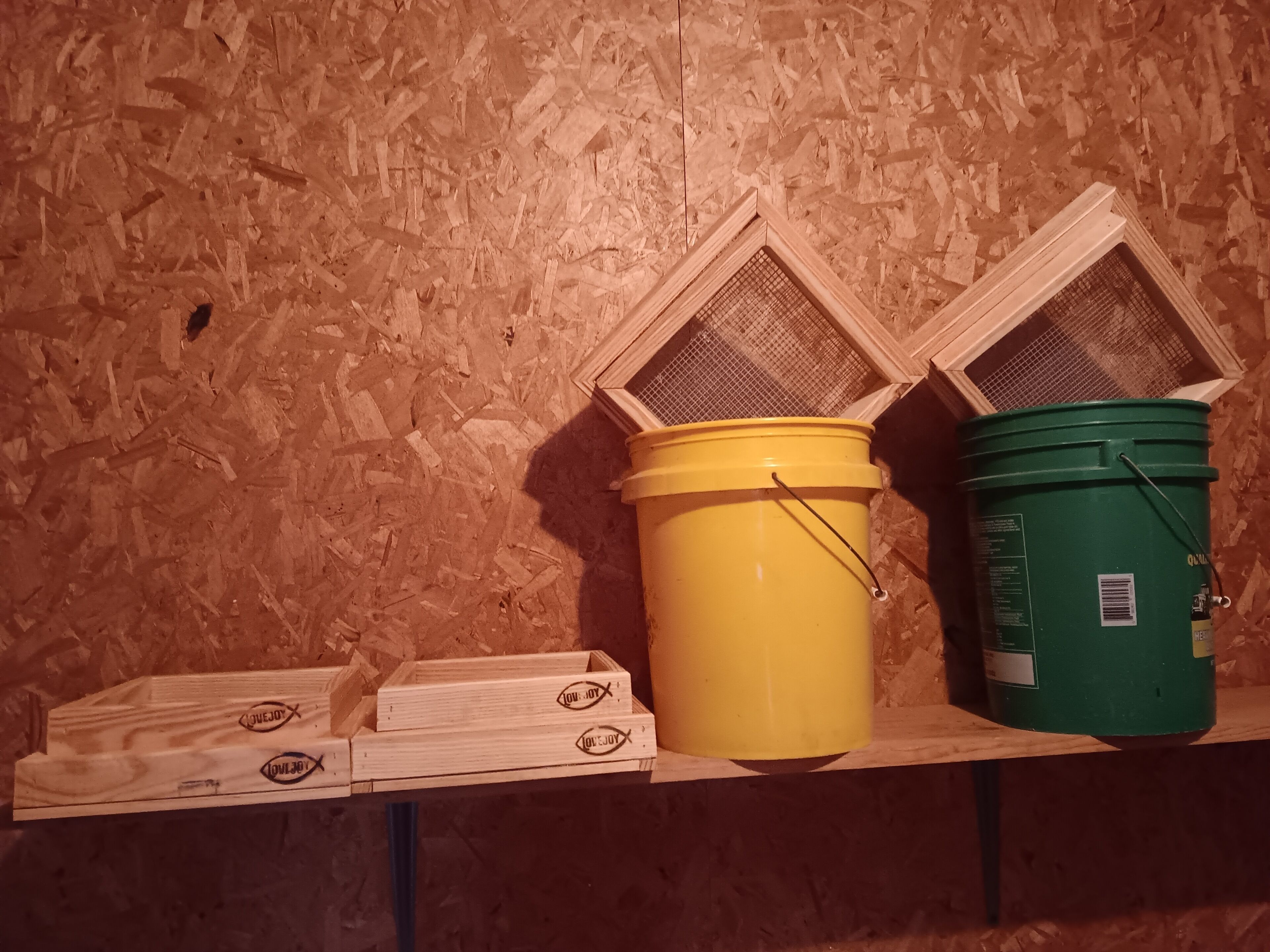 Two buckets on a shelf with wooden boxes below them.