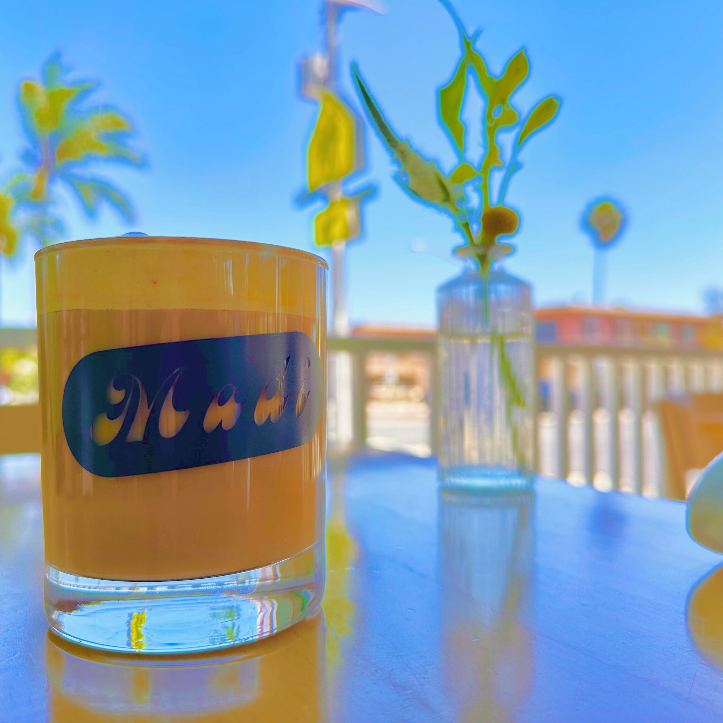 Ein Glas mit Etikett auf einem Tisch, eine Vase mit Blumen und unscharfer Hintergrund im Freien.