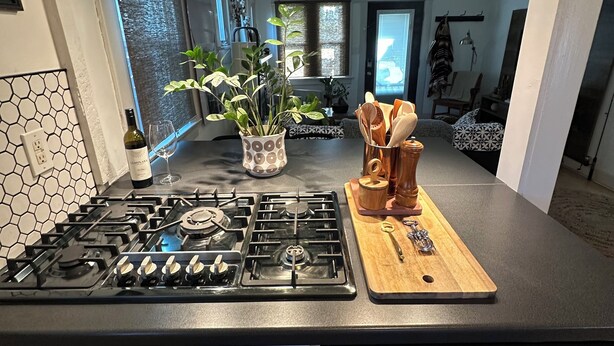 A modern kitchen with a gas stove, a microwave, and a dishwasher. There is a wooden cutting board with utensils on it, and a potted plant on the counter. - Beautiful Normal Heights Living (San Diego)