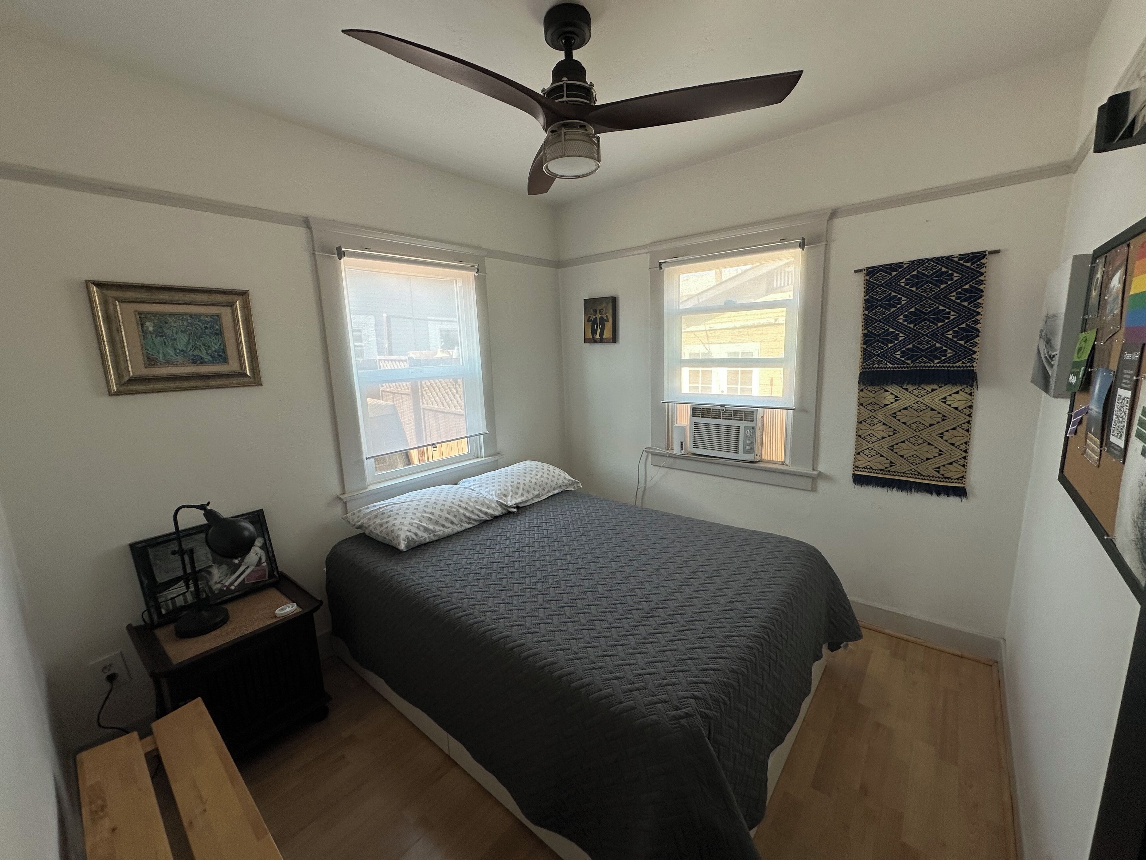 A bedroom with a bed, two windows, a ceiling fan, a nightstand, and a small table.